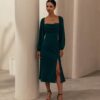Woman in green party wear midi dress with long sleeves and slit, standing indoors near a pillar