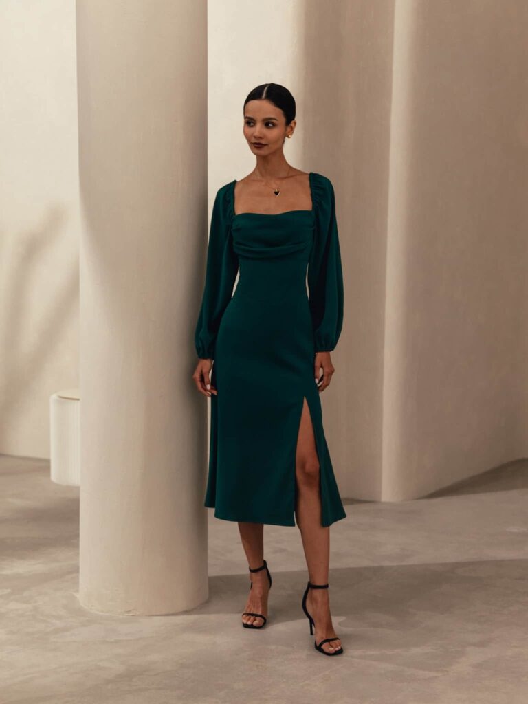 Woman in green party wear midi dress with long sleeves and slit, standing indoors near a pillar